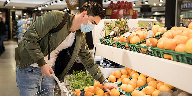 Alkohol und Corona junger Mann mit Gesichtsmaske sucht Früchte im Supermarkt aus