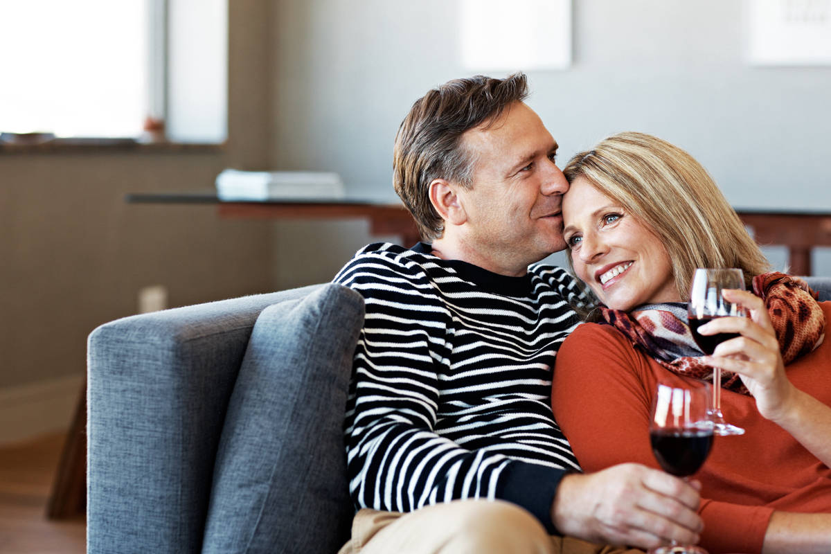 Ein Mann und eine Frau sitzen mit Rotweingläsern auf dem Sofa