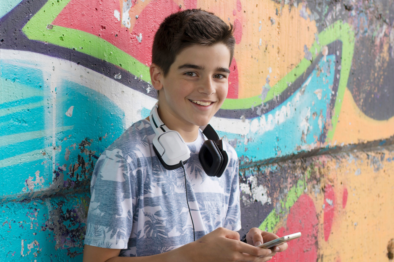 Ein steht mit einem Smartphone vor einer Grafitti-Wand.